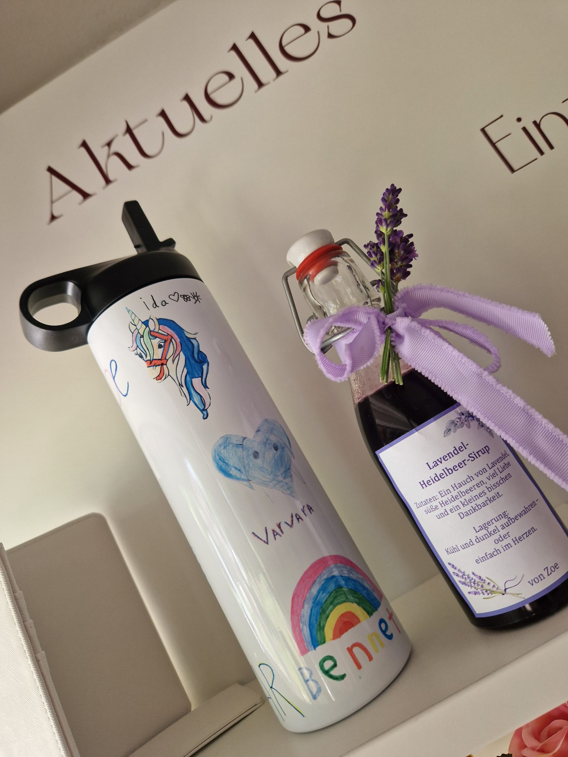 Eine weiße Thermoflasche mit bunten Kinderzeichnungen, als Abschiedgeschenk für Lehrer/Lehrerin Erzieherin